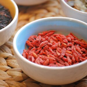 Close-up of goji berries and black rice in ceramic bowls on textured surface.
