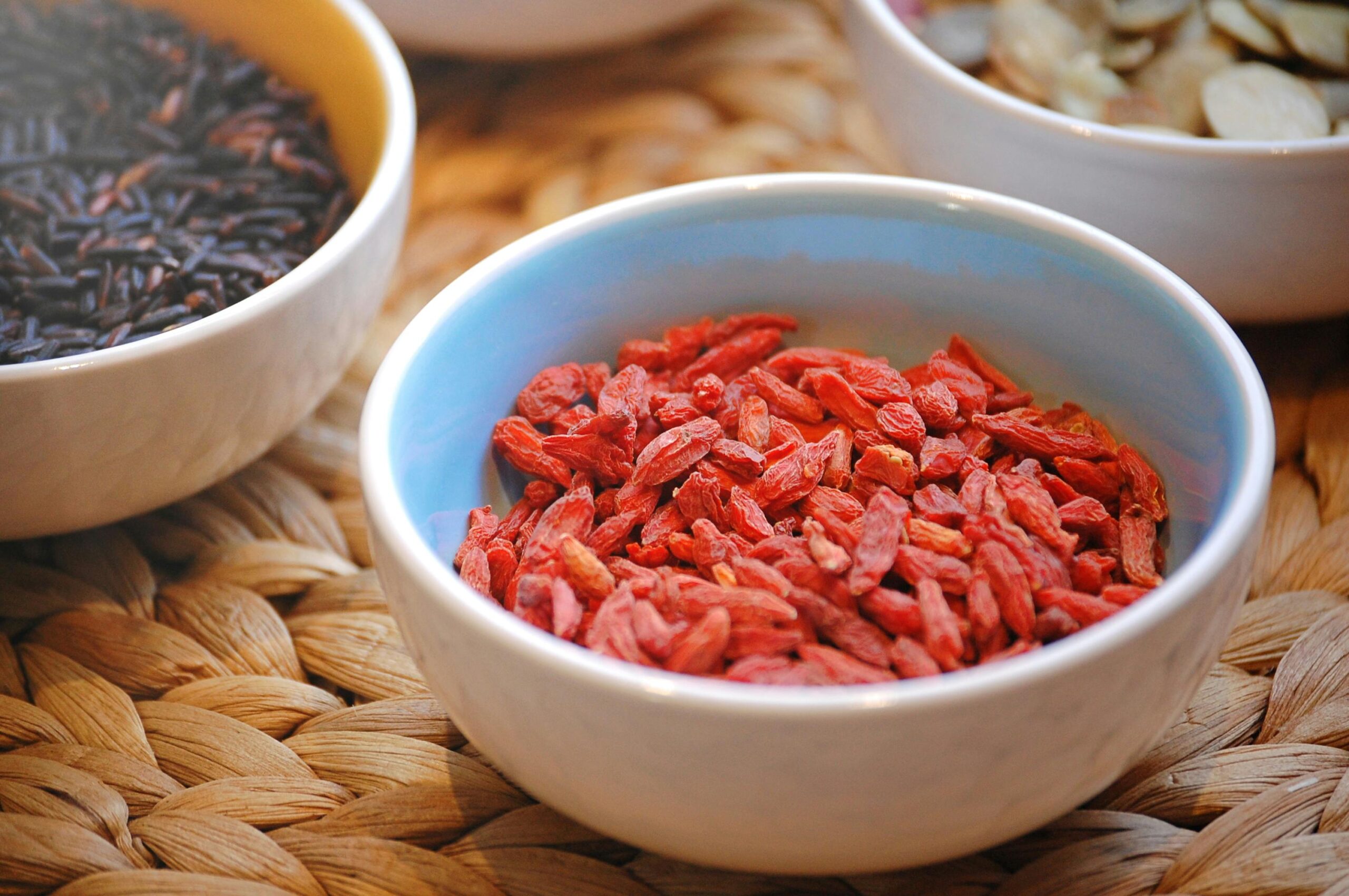 Close-up of goji berries and black rice in ceramic bowls on textured surface.