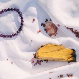 Amethyst bracelet, Palo Santo, and crystals arranged on white fabric for spiritual healing.