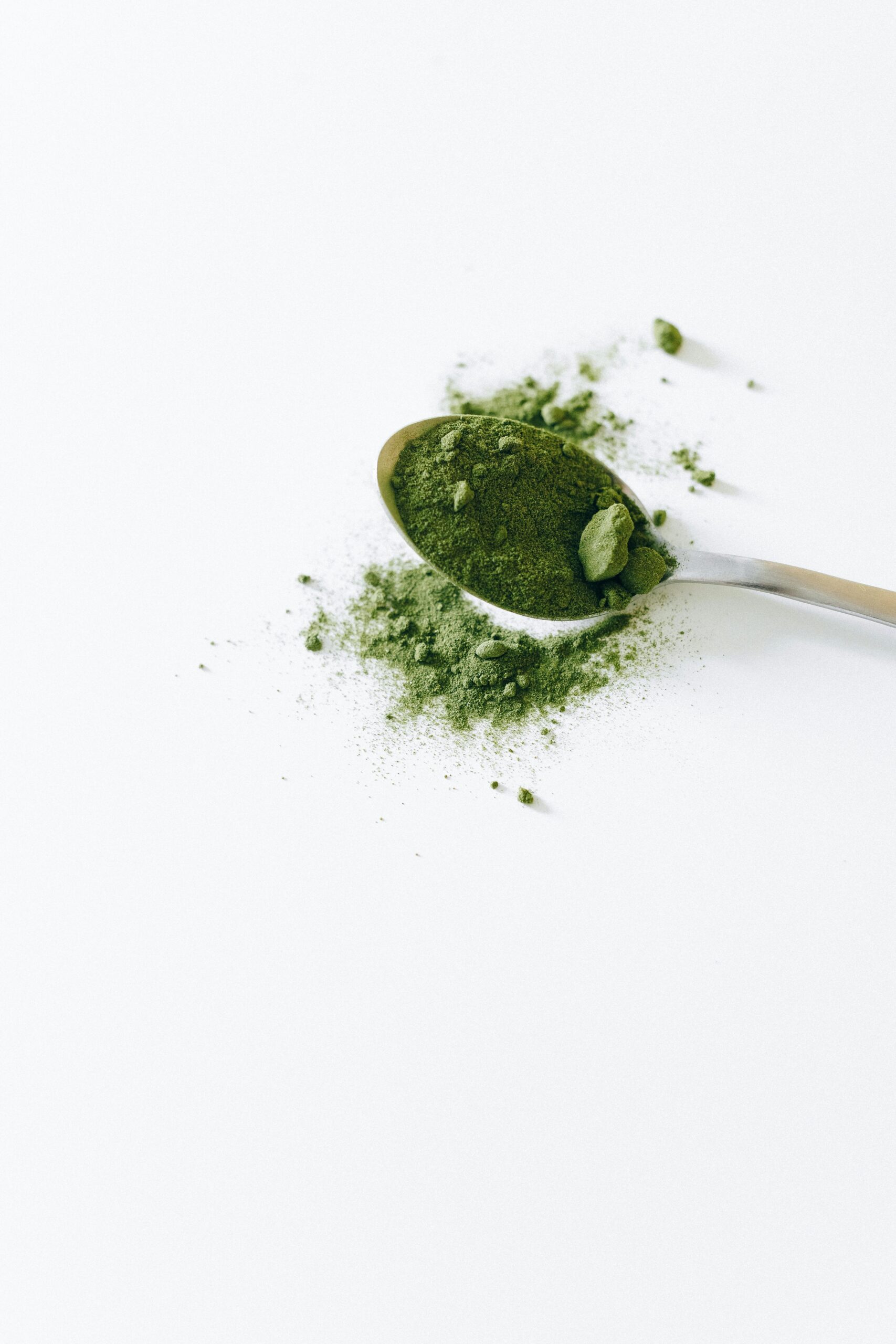 Top view of organic matcha powder on a silver spoon with a white background.
