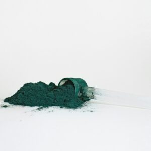 A pile of spirulina powder in a transparent measuring scoop isolated on a white background.