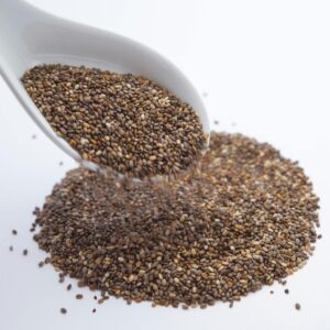 A close-up shot of chia seeds pouring from a white ceramic spoon onto a white surface.
