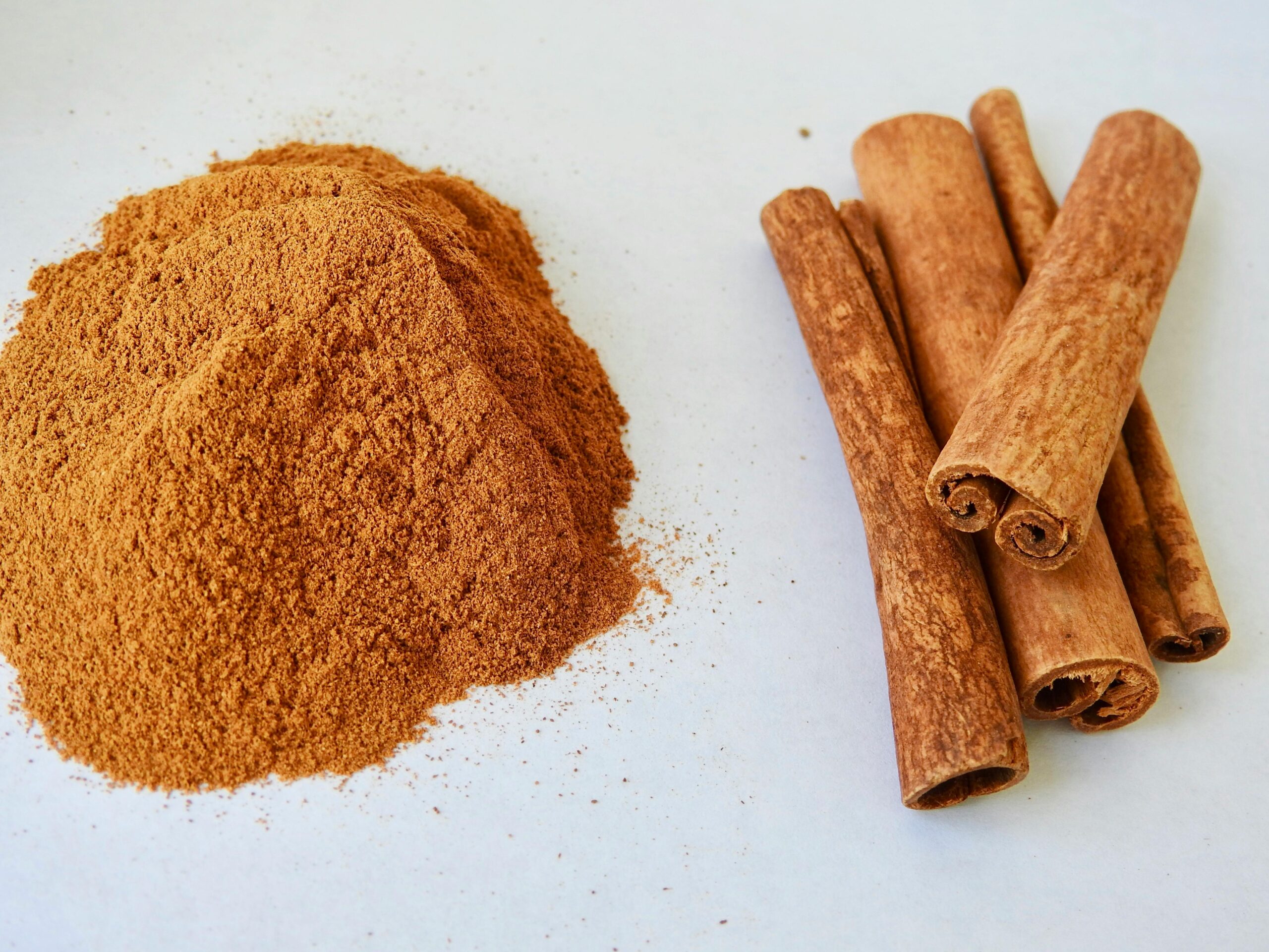 Close-up of aromatic cinnamon sticks and cinnamon powder on a white surface.