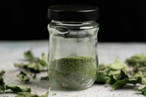 Close-up of a glass jar filled with dried, powdered mint leaves, ideal for culinary use.
