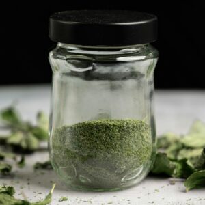 Close-up of a glass jar filled with dried, powdered mint leaves, ideal for culinary use.