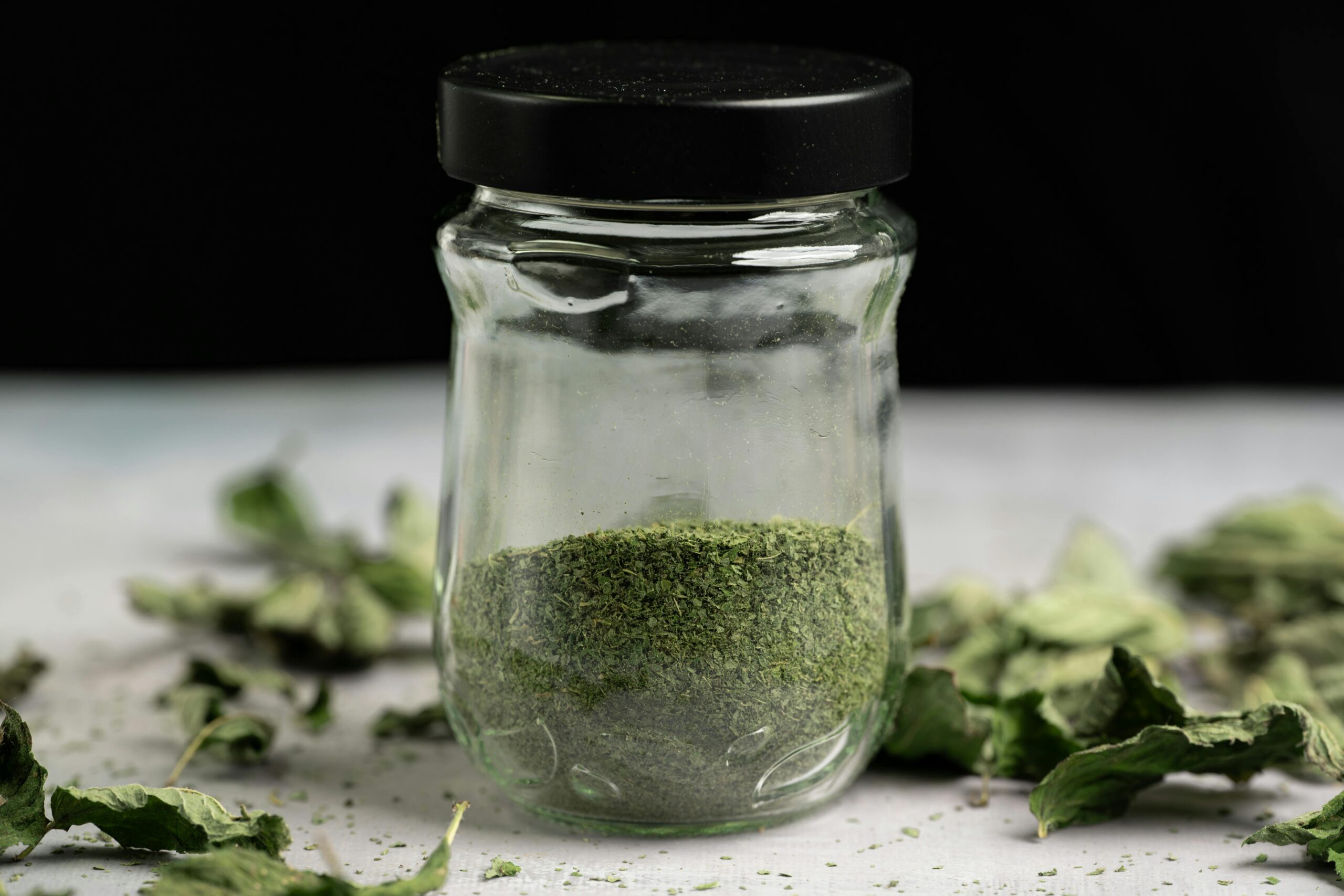 Close-up of a glass jar filled with dried, powdered mint leaves, ideal for culinary use.