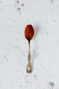 Top view of metal spoon with natural paprika powder spice placed on marble surface ready for healthy gourmet food preparing