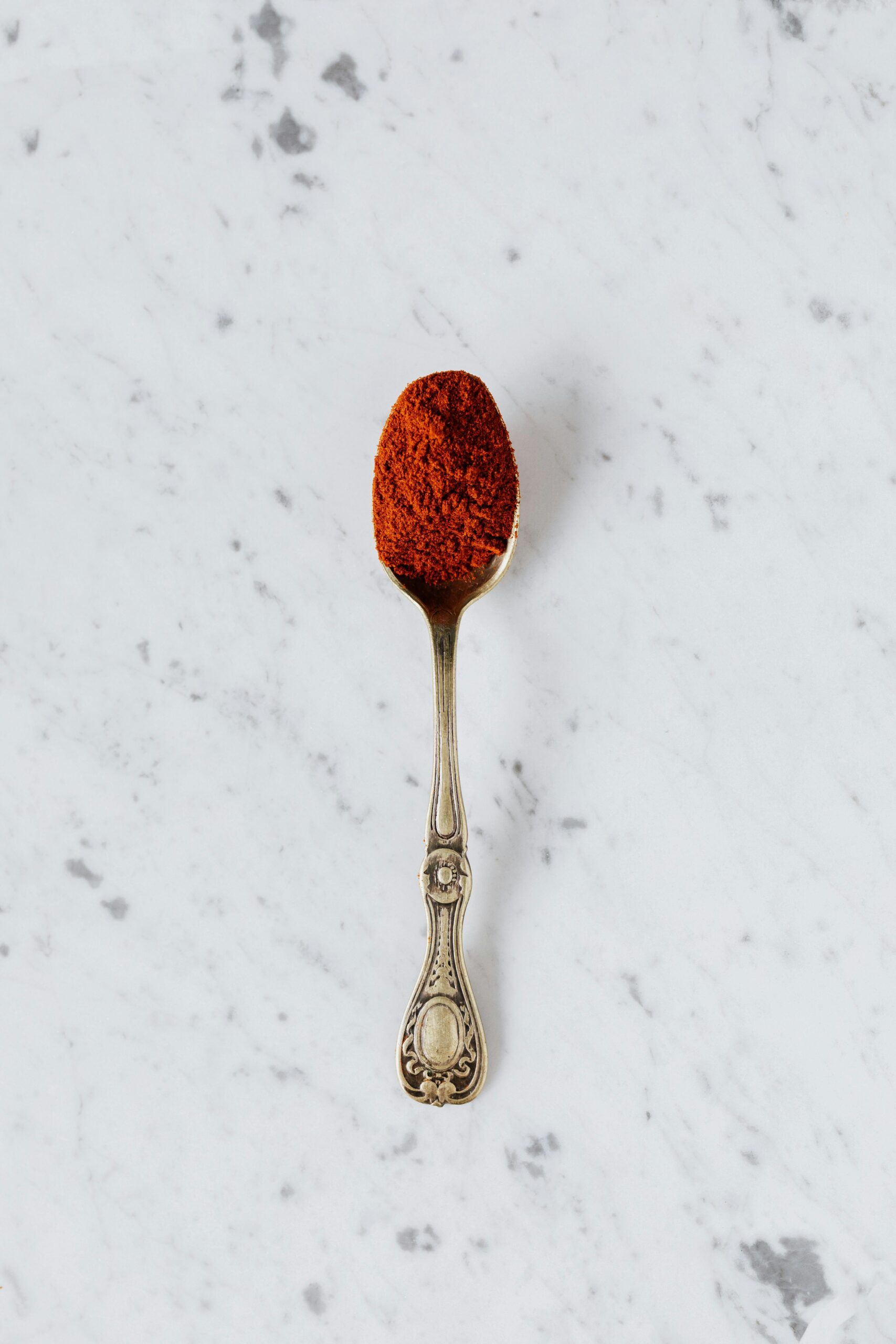 Top view of metal spoon with natural paprika powder spice placed on marble surface ready for healthy gourmet food preparing