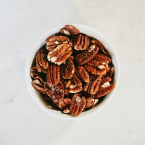 Top view of a bowl filled with healthy pecan nuts on a light surface, ideal for nutrition themes.