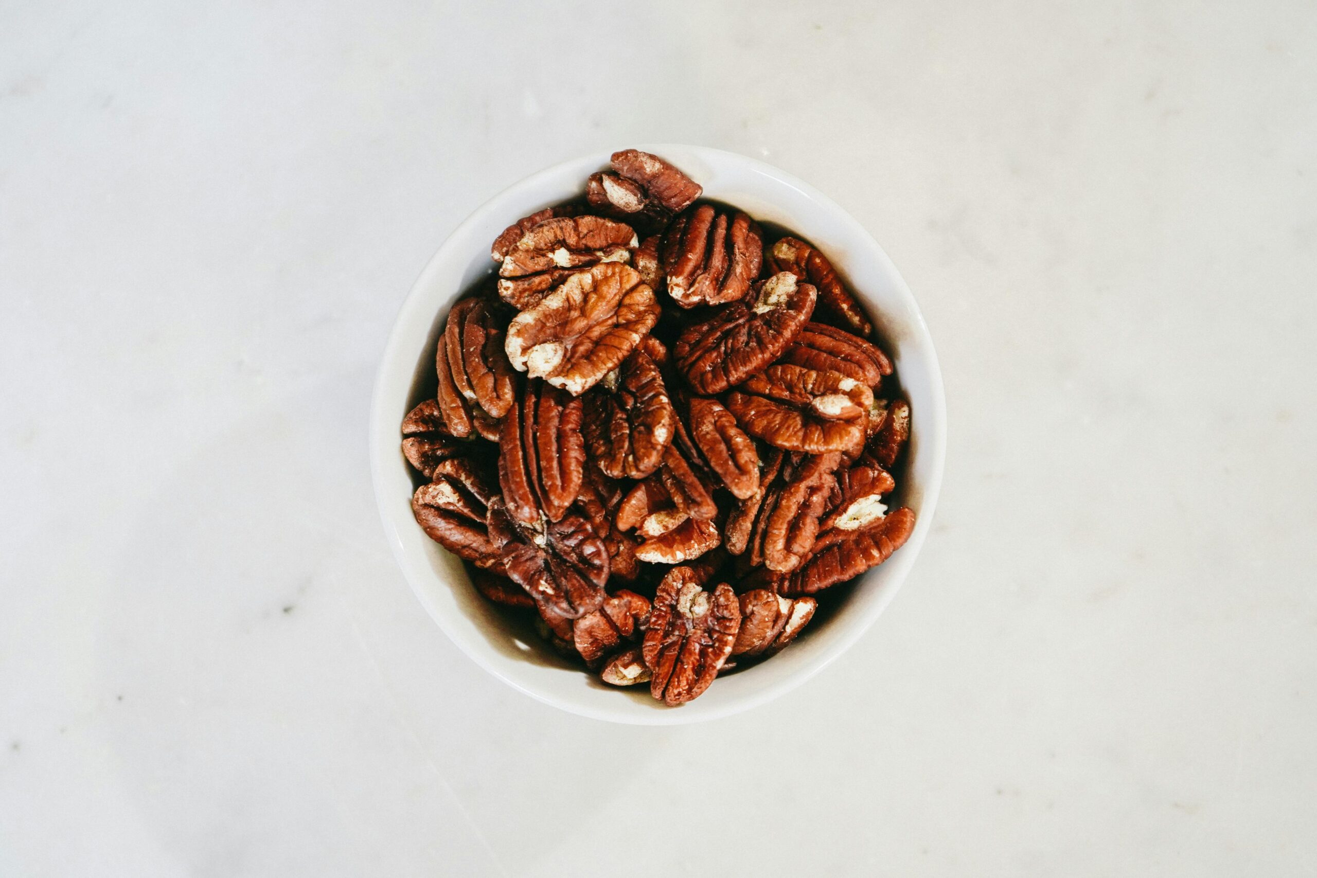 Top view of a bowl filled with healthy pecan nuts on a light surface, ideal for nutrition themes.