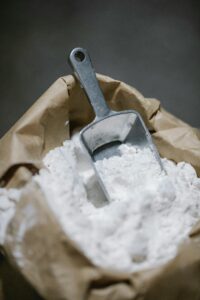 High angle stainless kitchen shovel placed in craft bag with heaped fresh flour in dark kitchen