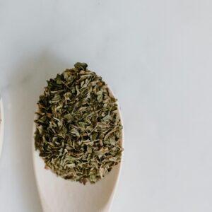 Close-up of dried herbs on wooden spoons against a white background, perfect for culinary use.