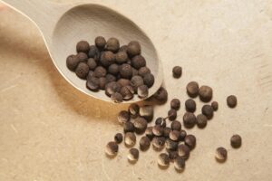 Close-up view of allspice peppercorns on a wooden spoon, perfect for culinary and spice themes.