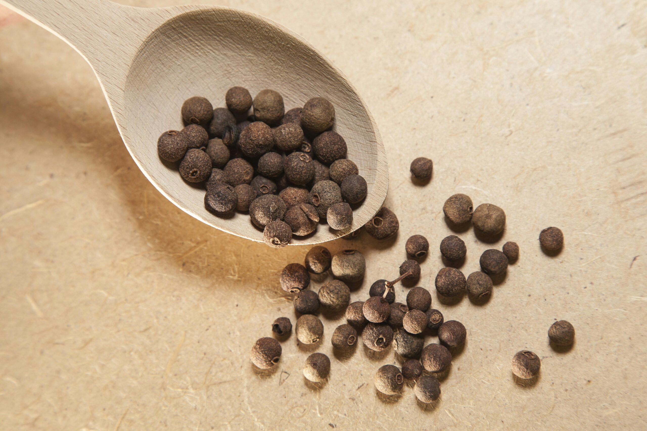 Close-up view of allspice peppercorns on a wooden spoon, perfect for culinary and spice themes.