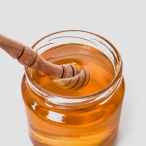Close-up of golden honey in a glass jar with a wooden honey dipper.