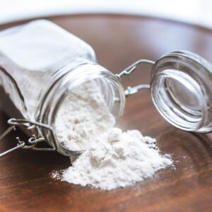 Glass jar tipped over with white flour spilling onto a wooden surface, ideal for baking themes.