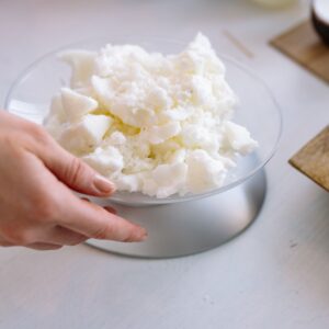 Close-up of a hand weighing candle wax indoors for crafting.